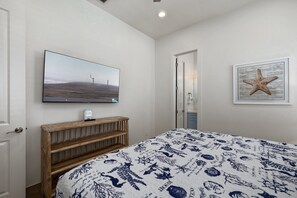 Une chambre à coucher avec un lit, un téléviseur fixé au mur, un banc en bois et un tableau encadré accroché au mur.