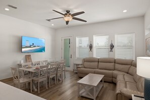 A living room with a television, a ceiling fan, a sofa, and a dining area with chairs and a table.