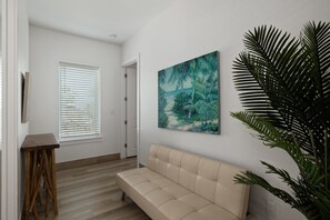 Ein Zimmer mit einem beigefarbenen Sofa, einem Gemälde mit einer tropischen Szene und einer großen Zimmerpflanze.