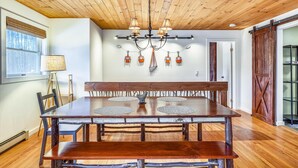 A dining area with a wooden table and benches, a chandelier, and a wall-mounted light fixture. - Stowe Sticks: 4 br, a/c, gas fireplace, firepit, deck! (Stowe)