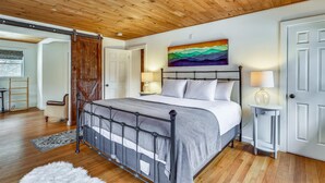 A bedroom with a metal bed frame, a wooden ceiling, a painting above the bed, and a white door. - Stowe Sticks: 4 br, a/c, gas fireplace, firepit, deck! (Stowe)