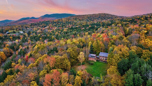 Una casa grande rodeada por un bosque con follaje otoñal.