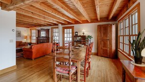 Un espacio habitable amplio con techo de madera, una mesa de comedor con sillas, un sofá y un ventanal con múltiples vidrios.