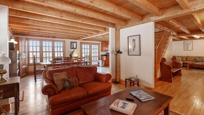 Un salón amplio con techo de madera, un sofá de cuero, una mesa de centro y un comedor con sillas y mesa de madera.