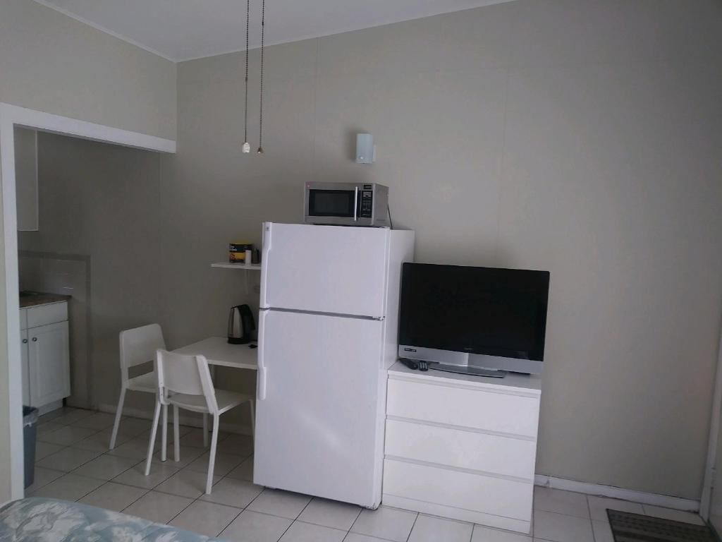 A compact room with a white refrigerator, a flat-screen TV, a small table, and a chair.