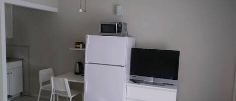 A compact room with a white refrigerator, a flat-screen TV, a small table, and a chair.