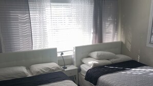 A bedroom with two beds, a nightstand, and a window with curtains.