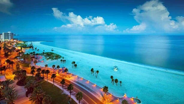 A coastal cityscape with a wide beach, palm trees, and a clear sky.