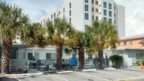 A modern hotel with a white facade, multiple floors, and a parking area with palm trees.