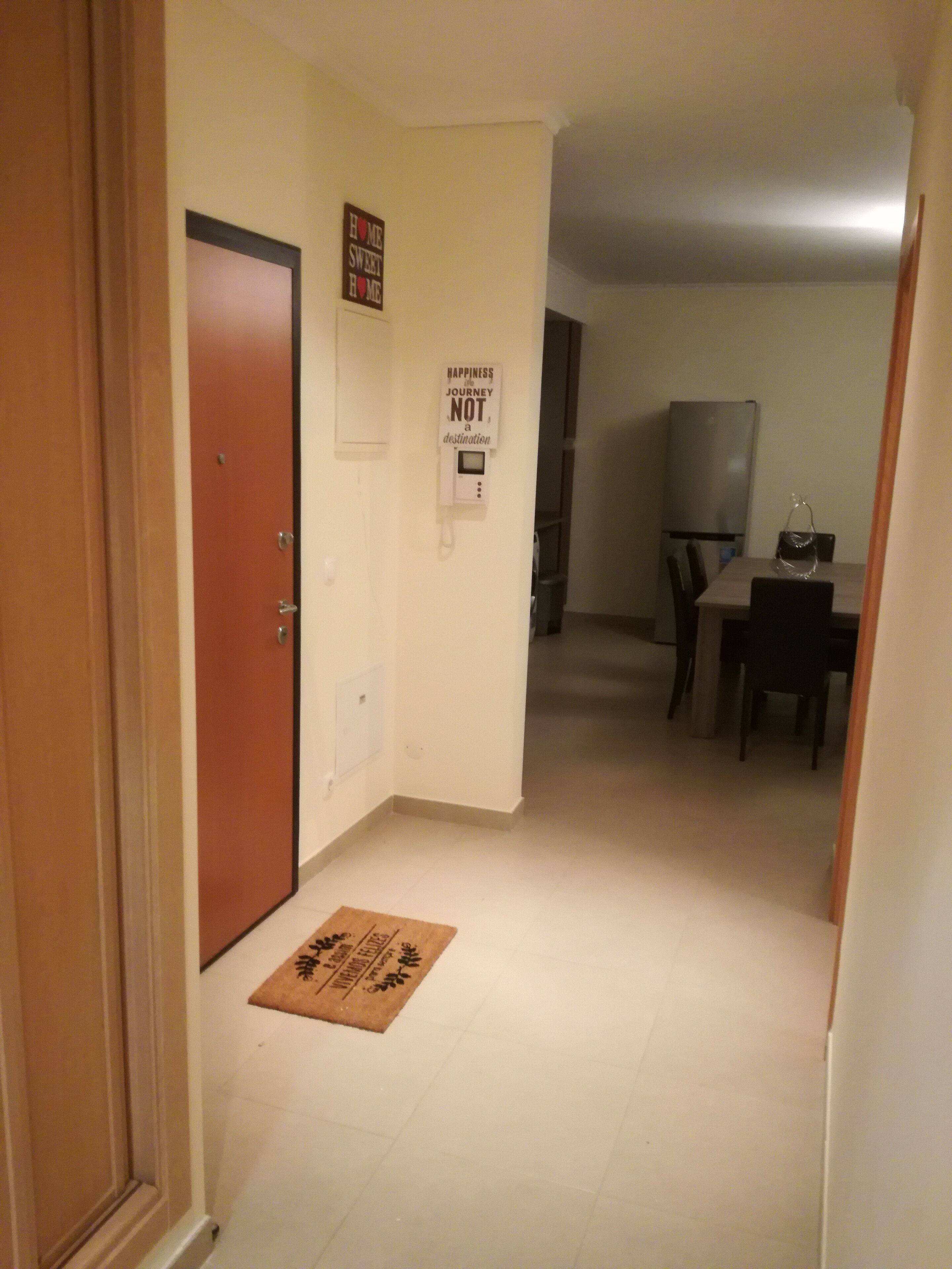 Ein Flur mit Holztür, Fußmatte, Kühlschrank und einem Esstisch mit Stühlen.
