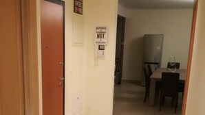 A hallway with a wooden door, a doormat, a refrigerator, and a dining table with chairs. - T2 Novo Alto do Quintão (Portimão)