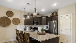 Una cocina moderna con armarios oscuros, encimera de granito, lámparas colgantes y una isla central con taburetes de bar.