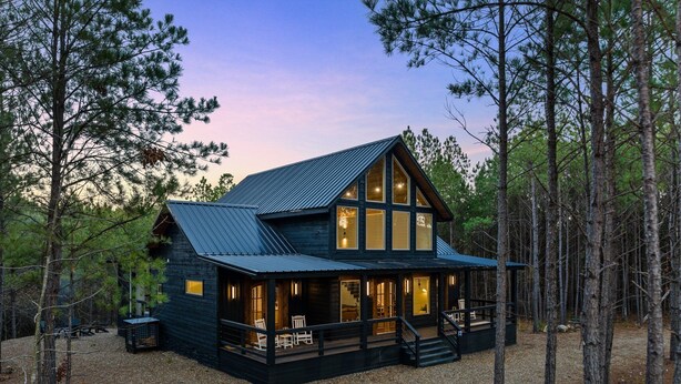 A cabin with a large porch, multiple windows, and a metal roof, surrounded by trees. - Play-Set, Darts, Large Back Deck, Hot Tub, Pets, Hidden Jewel (Broken Bow)