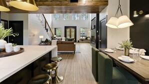A spacious kitchen with a central island, bar stools, and pendant lighting. A staircase leads to a living area with a fireplace and large windows. - Play-Set, Darts, Large Back Deck, Hot Tub, Pets, Hidden Jewel (Broken Bow)