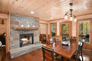 Ein Holzinterieur mit Kamin aus Stein, einem Esstisch und großen Fenstern.