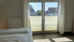 Un dormitorio con cama, un radiador, una ventana con persianas y vistas a casas.