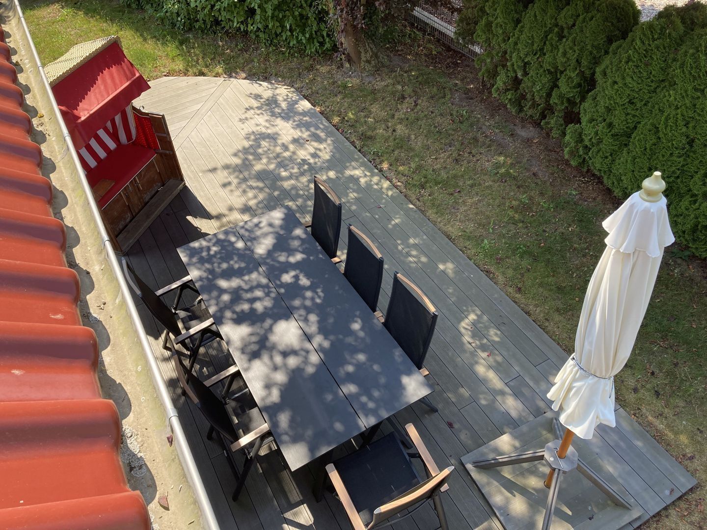 Terraza con mesa y sillas, rodeada de follaje y un paraguas blanco.