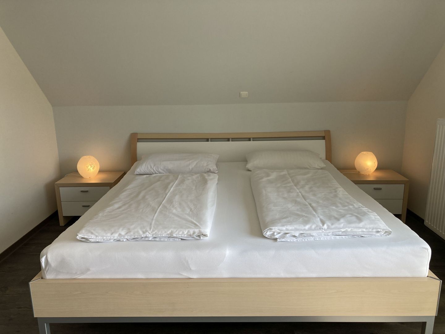 A double bed with white linens, two bedside tables with lamps, and a wooden headboard.