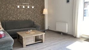 Una sala de estar con un sofá gris, una mesa de centro de madera, una lámpara y un radiador.