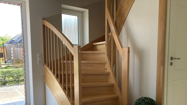 Una escalera de madera con barandilla, una planta en maceta y una puerta.