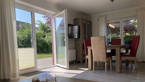 Una habitación con una mesa de madera, sillas, un televisor y un ventanal corredero a un balcón.