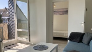 A modern living room with a sofa, a coffee table, and a sliding glass door leading to a bedroom.
