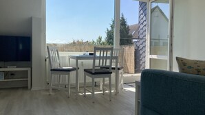 A room with a TV, a dining table with chairs, a sofa, and a sliding glass door leading to an outdoor area.