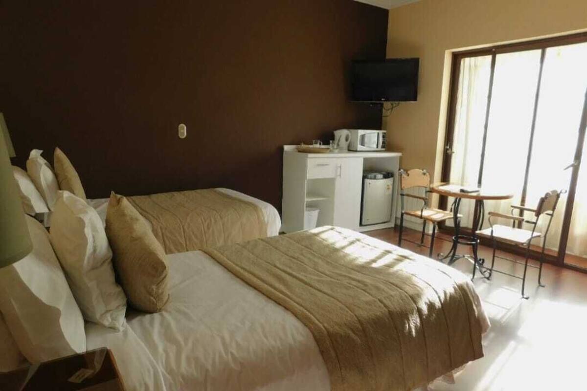 Quarto de hotel com uma cama, uma escrivaninha com televisão e uma cadeira.