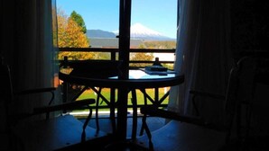 A room with a table and chairs near a window with a view of a mountain.