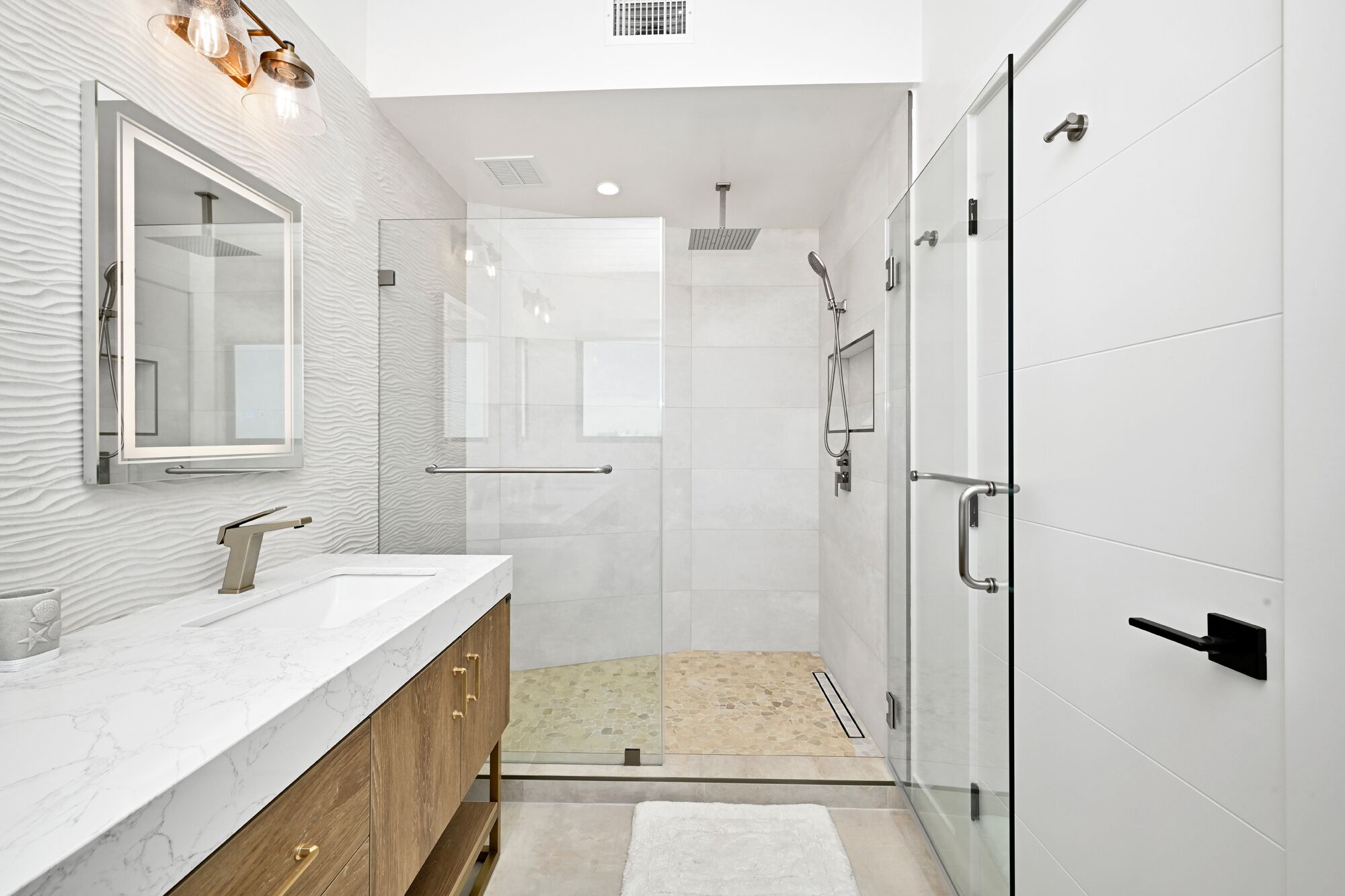 A modern bathroom with a marble vanity, a glass shower enclosure, and a white tiled floor.