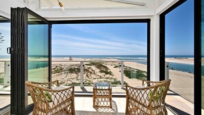 Ein Balkon mit Korbstühlen und einem Glastisch mit Blick auf einen Strand und einen Rettungsturm.
