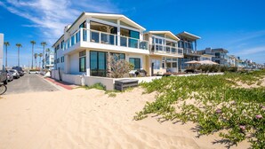 Ein modernes Strandhaus mit zwei Etagen, einem Balkon, einer Auffahrt und einem Sandstrand im Vordergrund.