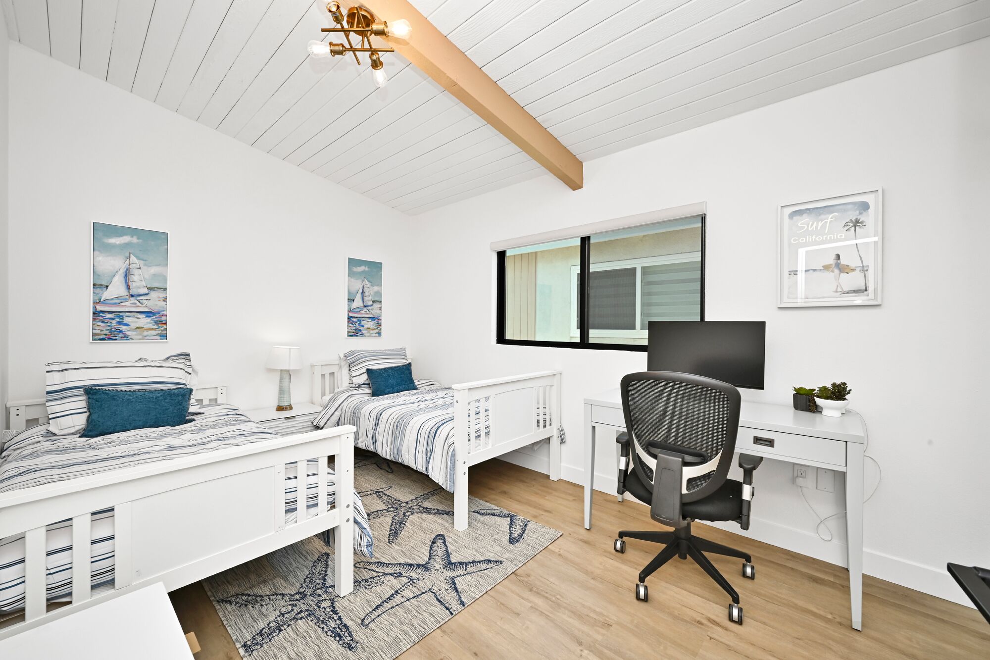 Een slaapkamer met twee bedden, een bureau en een computer. Er liggen vloerkleden met een zeesterrenpatroon en er is een plafondlamp.