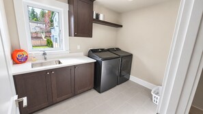 Una cocina compacta con lavavajillas integrado, ventana con vistas a un jardín trasero y un lavabo blanco.