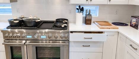 A modern kitchen with stainless steel appliances, white cabinetry, and a window with a view.