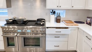 Cozinha moderna com eletrodomésticos de aço inoxidável, armários brancos e janela com vista.