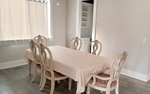 Un comedor con mesa y sillas, una ventana con cortinas y una puerta que da a un armario.
