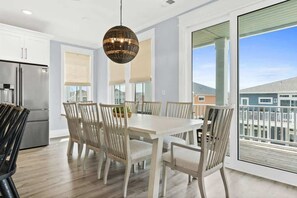 A modern kitchen with a dining area, large windows, and a view of the neighborhood. - Blue Heaven by Brunswick Vacation Rentals: Home with Heated pool & Beach Club (Ocean Isle Beach)