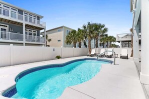 A swimming pool with a curved edge, surrounded by a white wall and palm trees.
