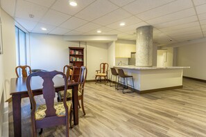 A spacious room with a dining area, a bookshelf, and a kitchen area.