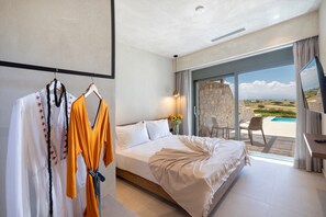 A hotel room with a large bed, a desk, a TV, and a view of a pool and landscape. - Dedalos Touch Boutique Hotel (Rethymno)