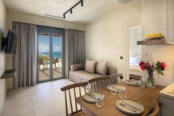 Habitación de hotel moderna con comedor, sofá, televisor y vista al mar.