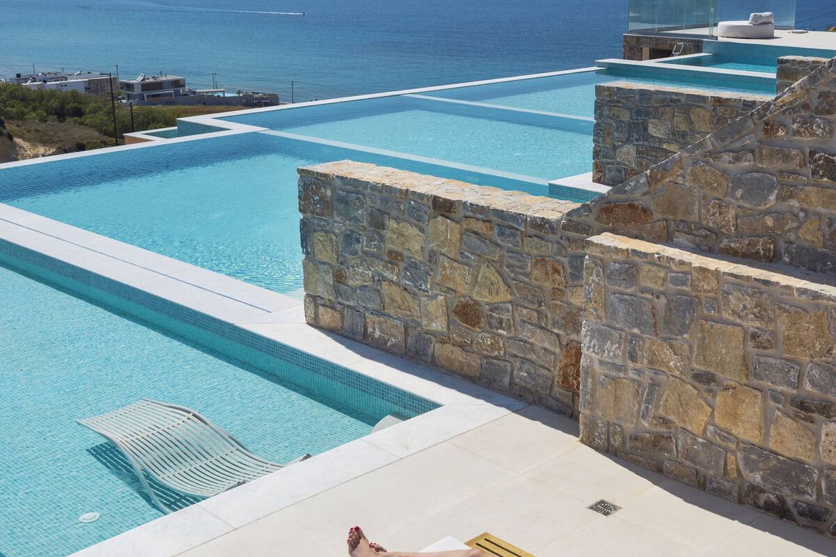 Una persona descansando en una tumbona junto a una piscina con vista al océano.