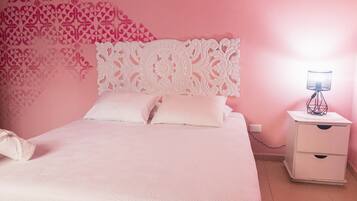 A bedroom with a bed, white nightstand, and a decorative wall piece.