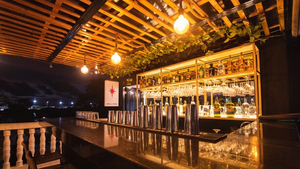A bar area with a wooden ceiling, hanging lights, and a bar stocked with bottles and glasses. - San Felicin Hostel (Cartagena)