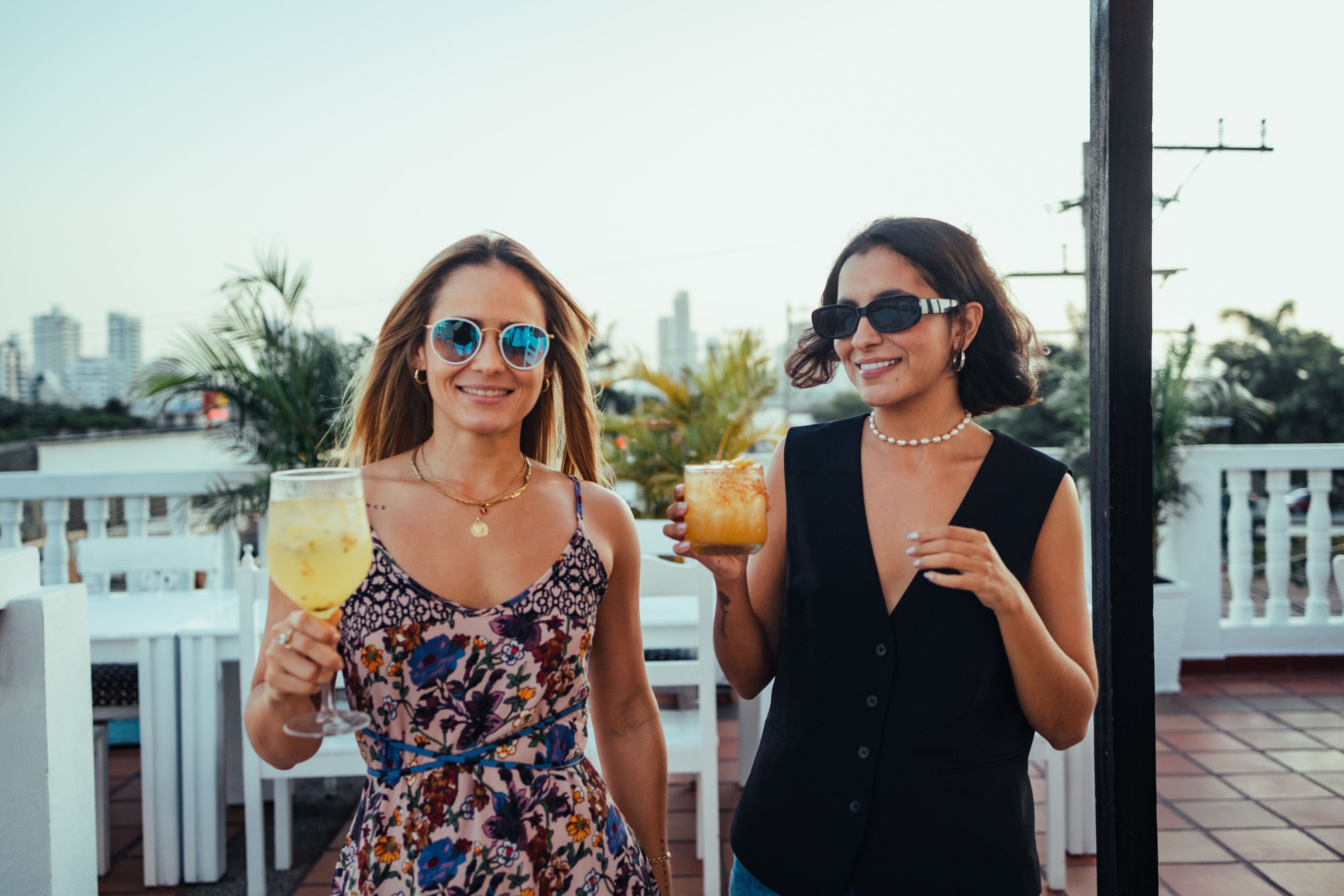 Two people holding drinks on a terrace with a city skyline in the background.