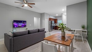 A modern living room with a sofa, dining table, and chairs, a TV mounted on the wall, and a ceiling fan. - Lovely Newly built condo centrally located in TPA
 (Tampa)
