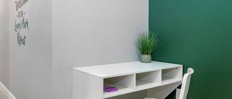 Un bureau blanc avec des étagères, une chaise blanche, une plante en pot et un mur orné d’une pancarte indiquant « Bienvenue chez… ».