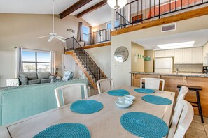A spacious living area with a dining table set for four, a sofa, and a staircase leading to an upper level.