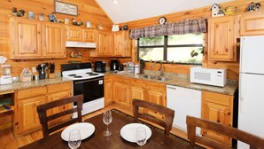 Cocina de cabaña de madera con encimeras de granito, estufa, lavabo y ventana con un adorno a cuadros.